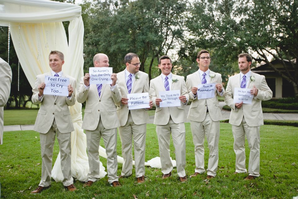 Groomsmen waiting at the alter holding up cute saying signs 