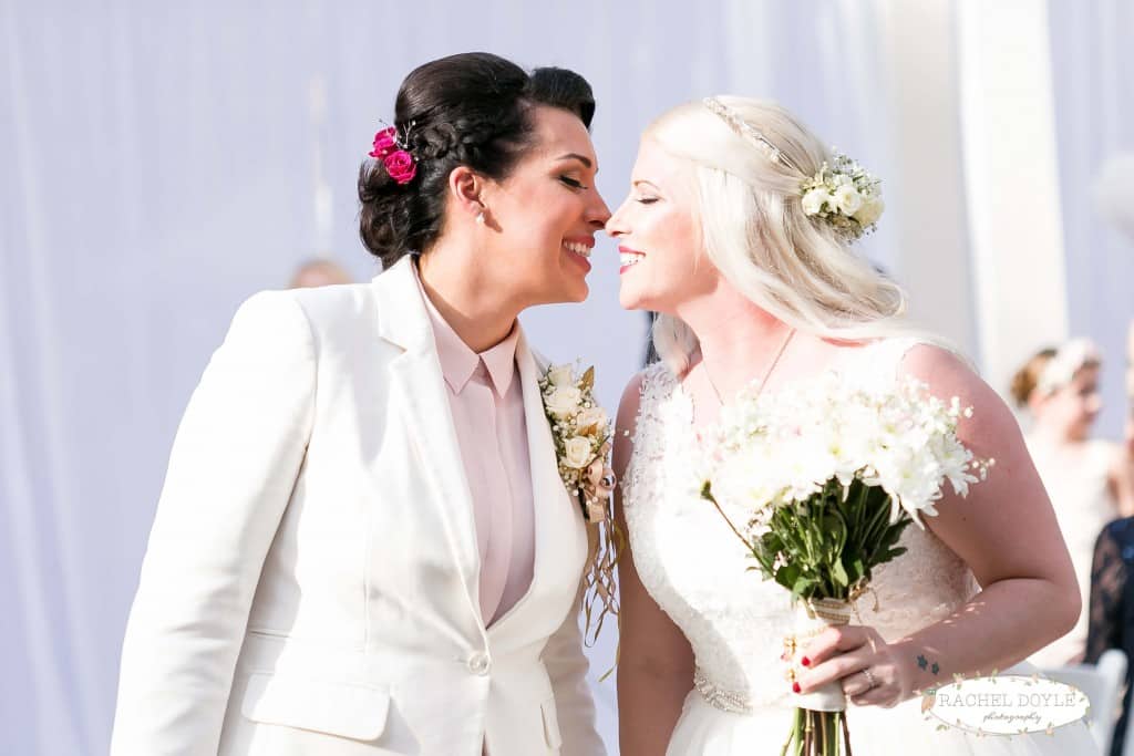 Same sex orlando wedding at wedding ceremony. Lace wedding dress. Floral wedding hair pieces. Half up half down wedding hair style. White flower bouquet. 