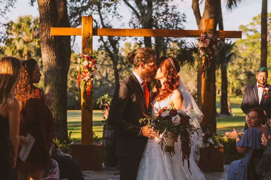 Bride and groom kiss at ceremony at Up the Creek Farm. Wooden wedding arch. 