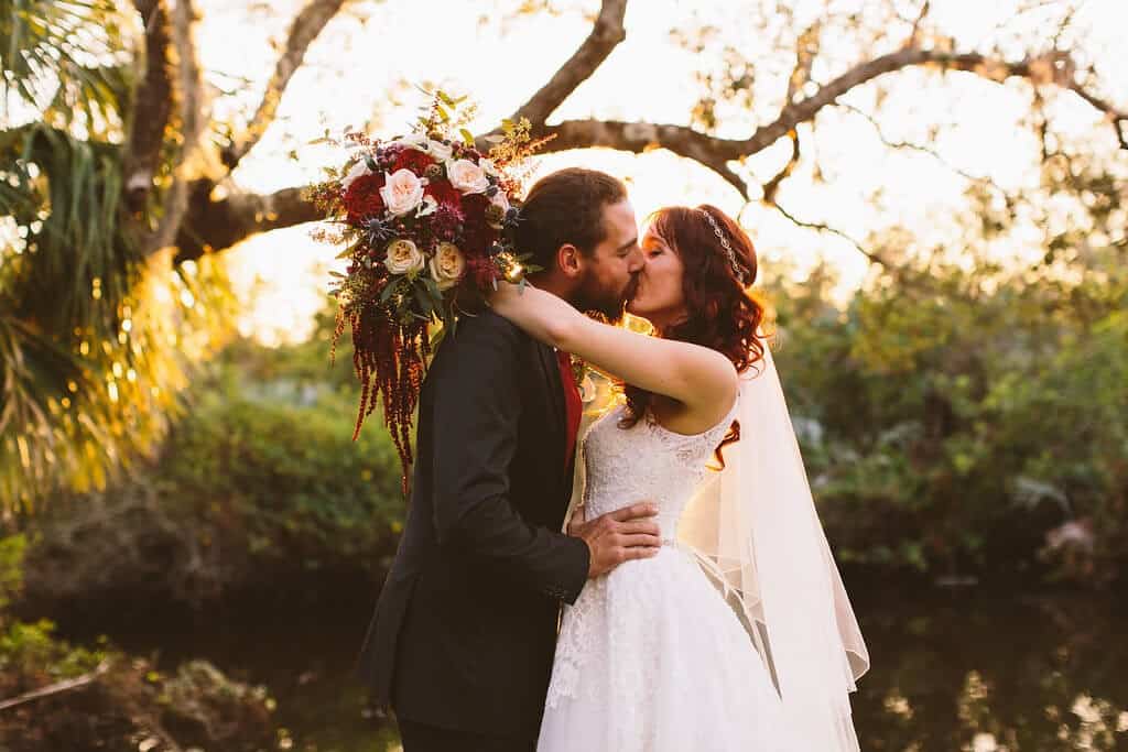 Bride and groom kiss at Up the Creek Farm. Lace wedding dress. Black wedding tuxedo. Pretty flower bouquet. 