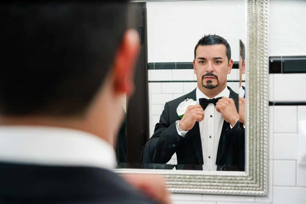 groom tying bow tie in the mirror