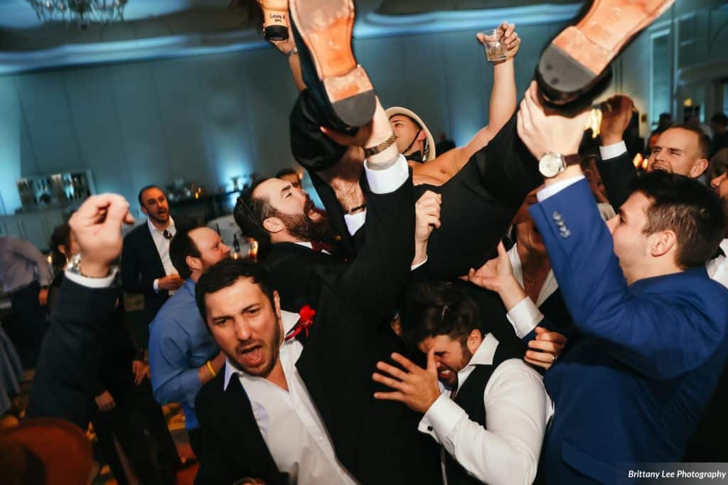 excited wedding guests lifting groom on their shoulders
