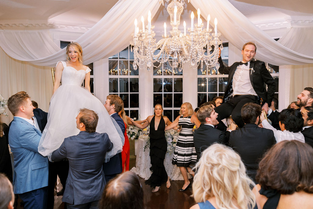 bride and groom on chairs being lifted by wedding guests