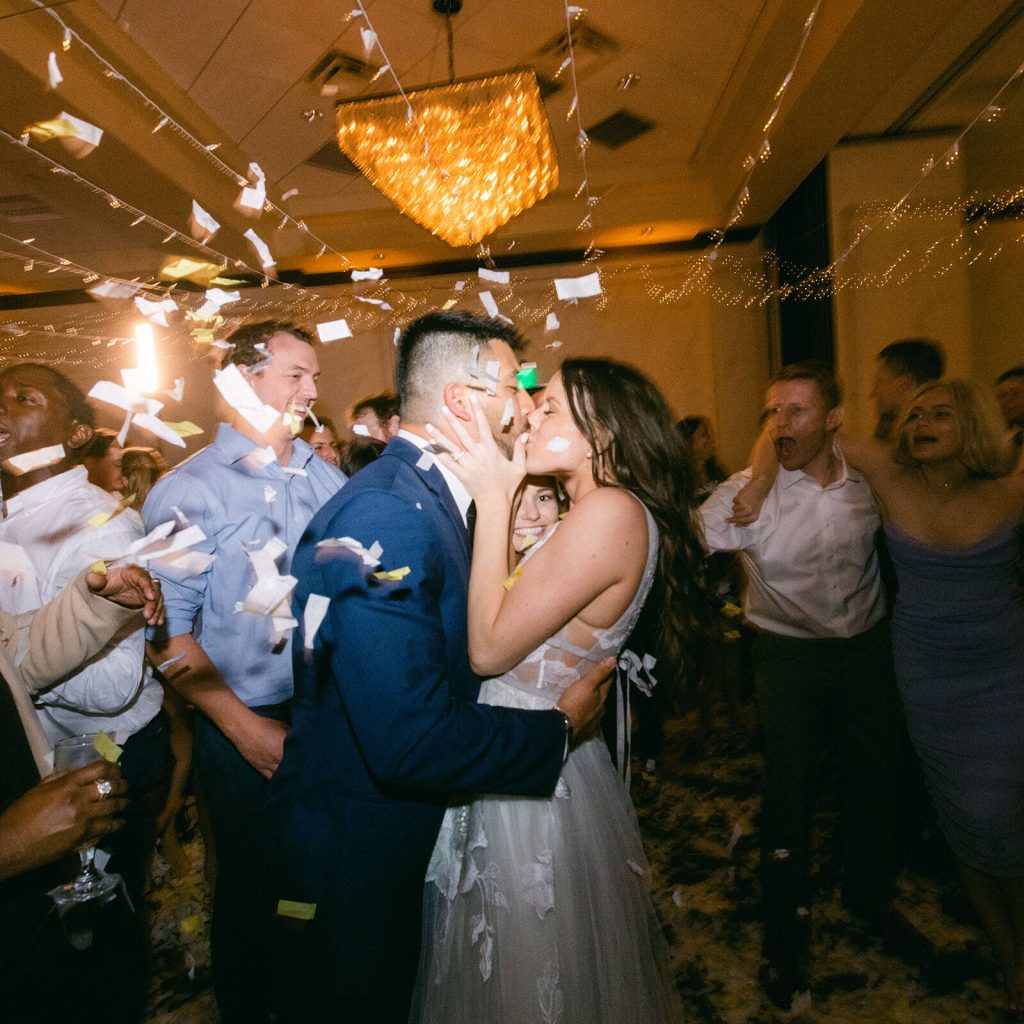 Bride and groom kissing surrounded by friends and family during the last dance of their wedding