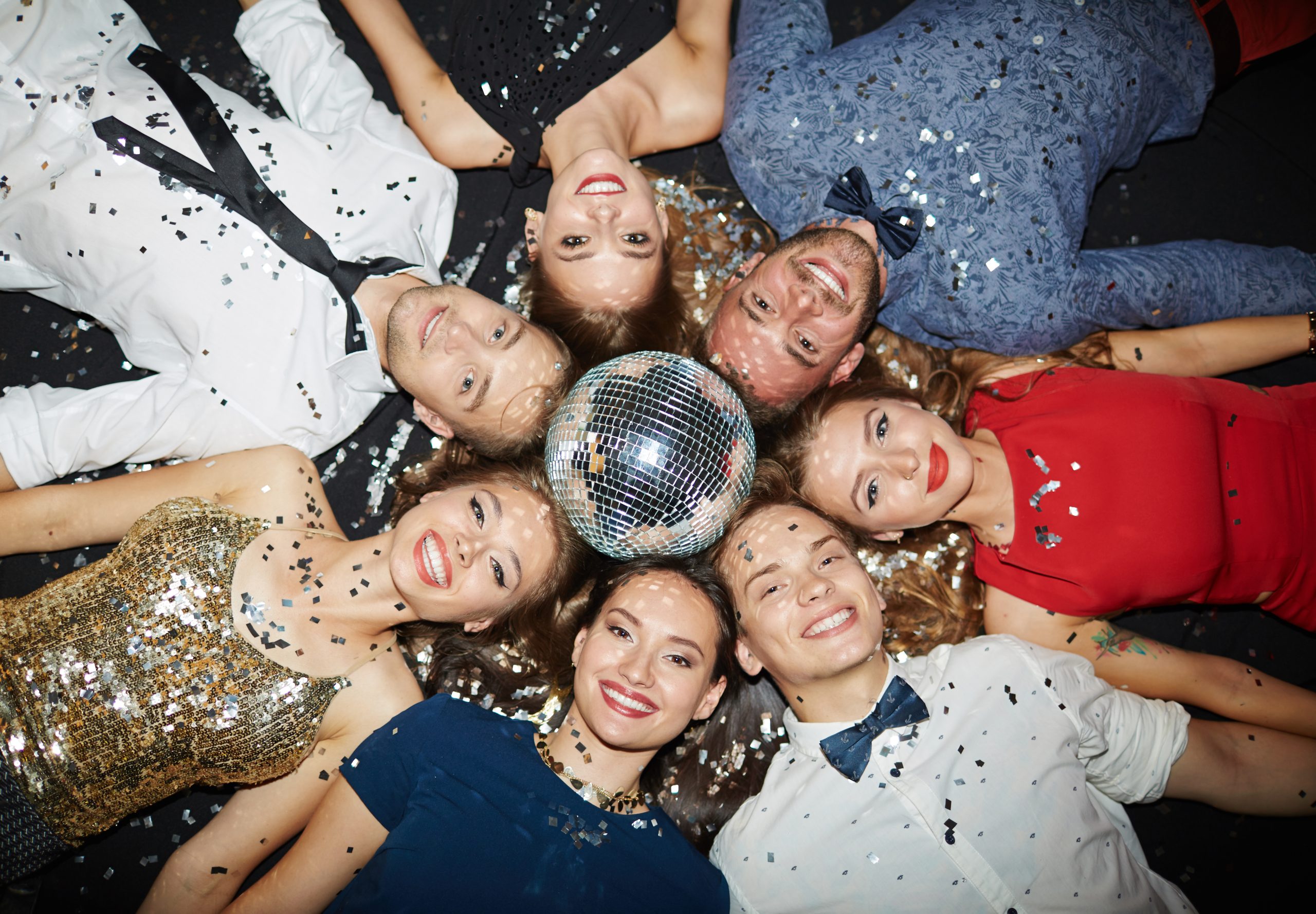 teens in formal dress laying with heads together around a disco ball
