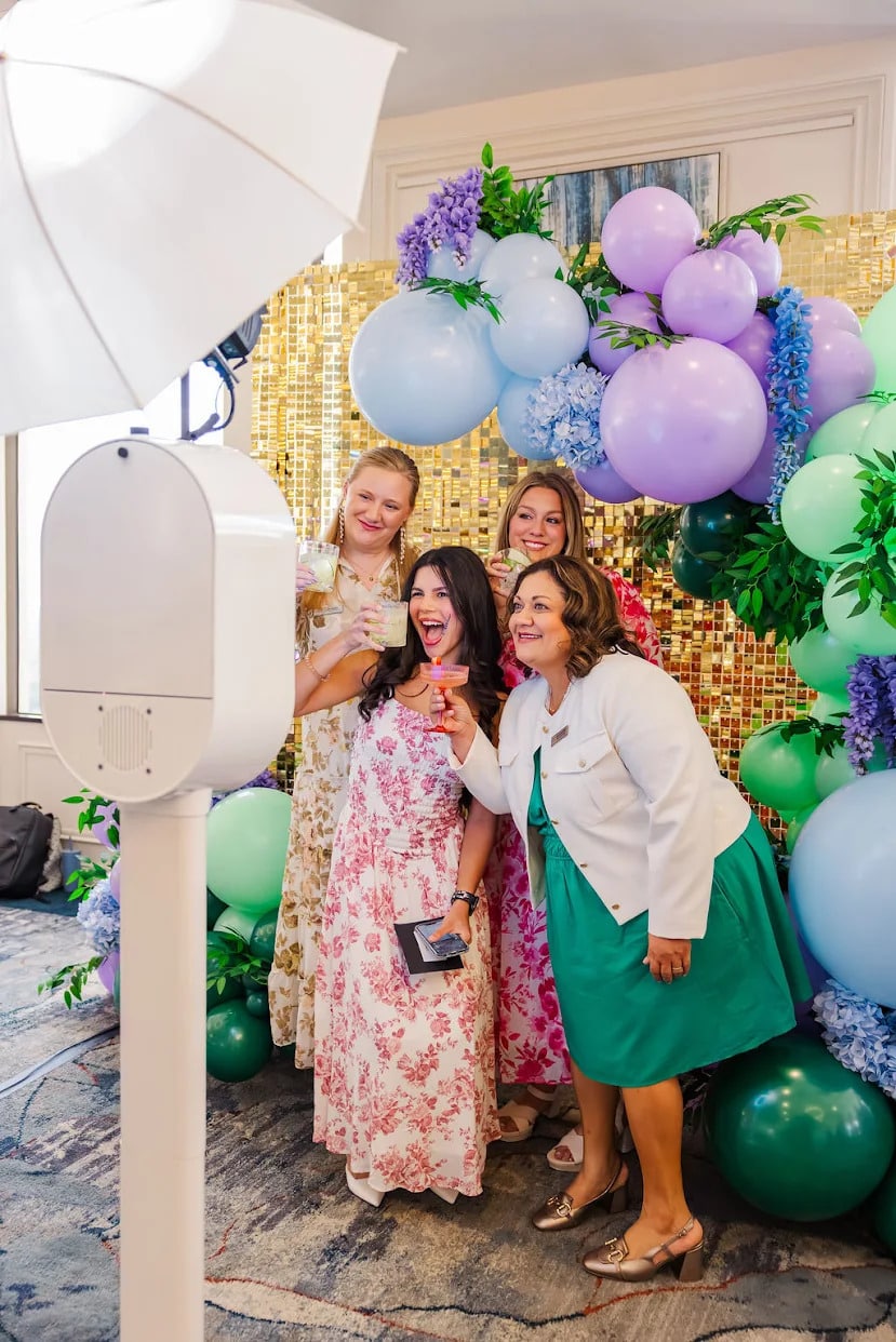 Happy women posing for picture in photo booth with balloon backdrop