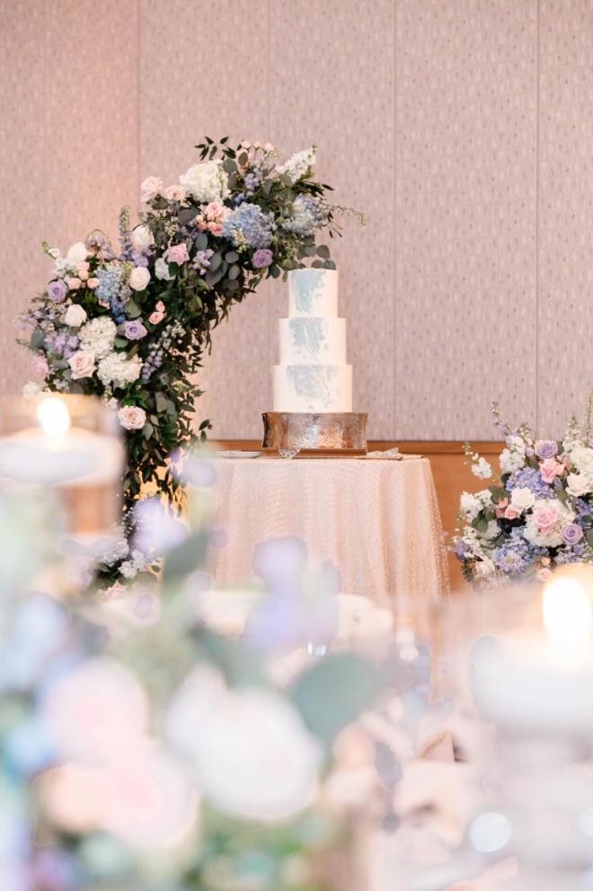 Tiered wedding cake framed by a pastel floral arch