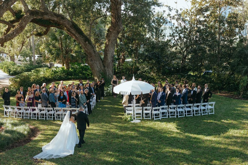 Bride and her father walking down the aisle at an outdoor ceremony at Victoria 1883 in New Smyrna Beach