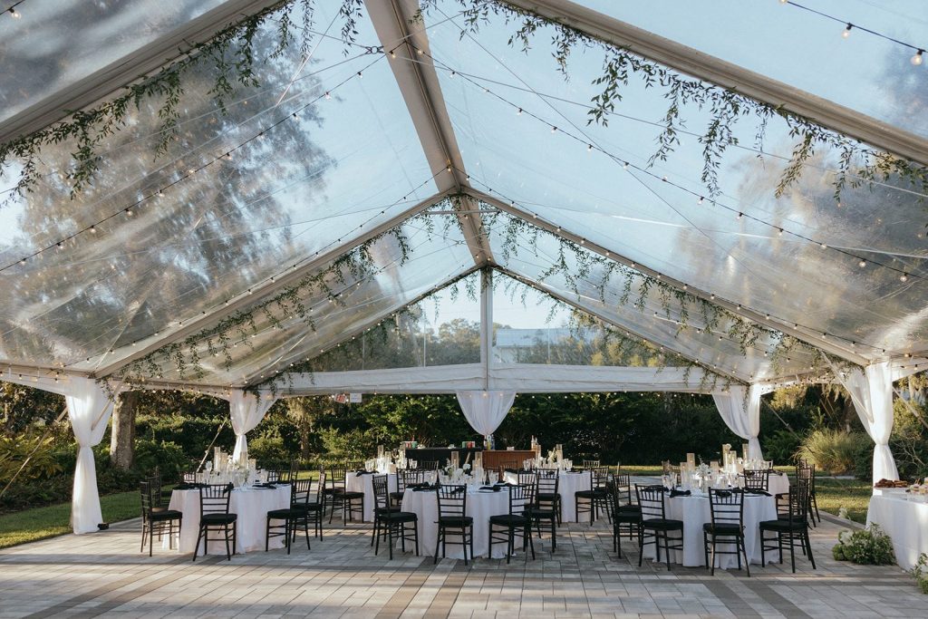 Clear-top reception tent with greenery and string lights at Victoria 1883, a New Smyrna Beach wedding venue