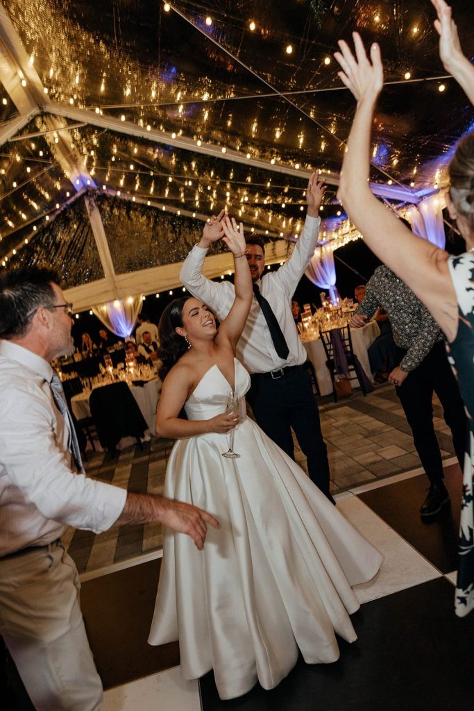 Bride dancing with guests and champagne under the string lights at a Victoria 1883 wedding reception